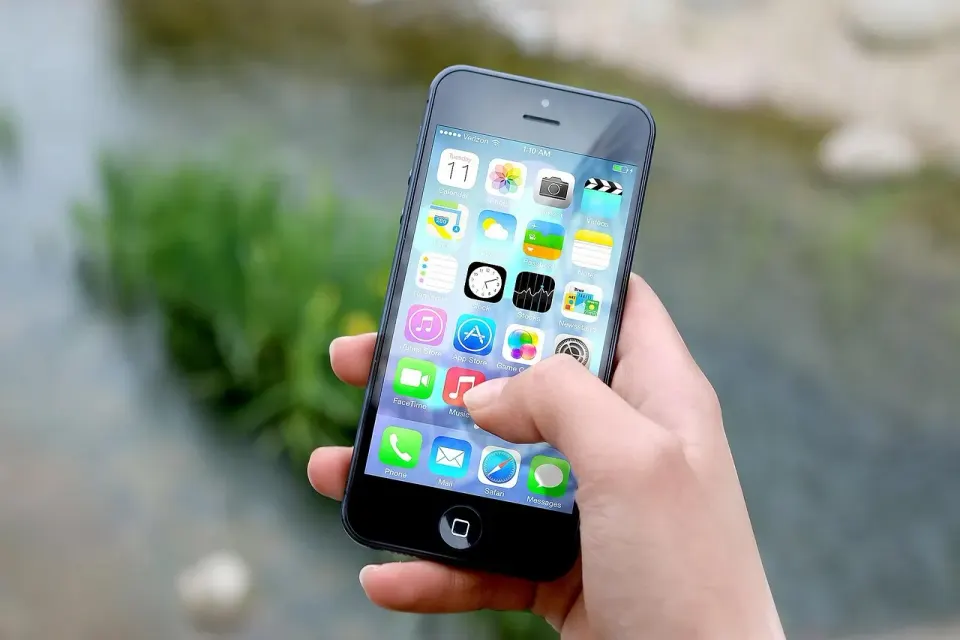 A hand holding a smartphone, the screen where a spoofed caller ID or Scam Likely label appears