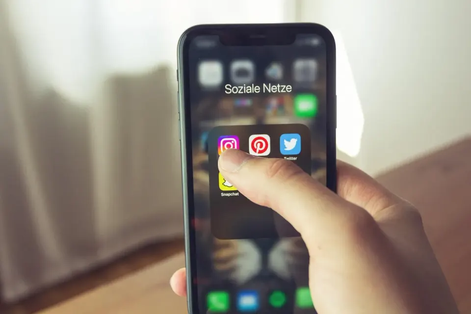 A hand holding a smartphone with apps on screen, ready to report and delete a scam text