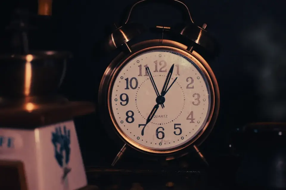 A coffee cup and grinder next to an old clock, the sort of household clock that never updates itself