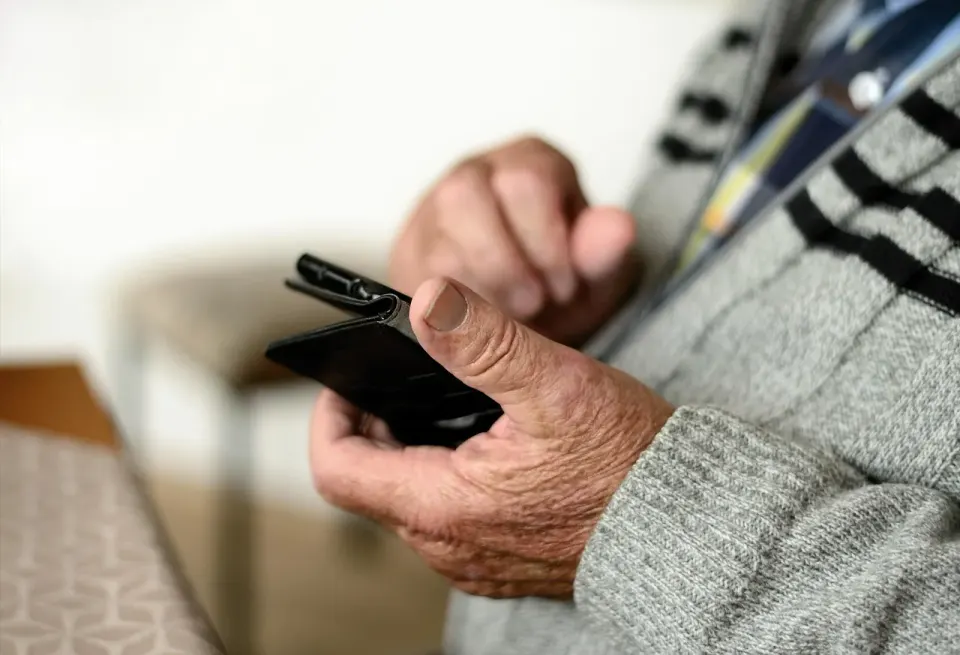 An older person holding a phone in a folio case, a device kept long after launch day